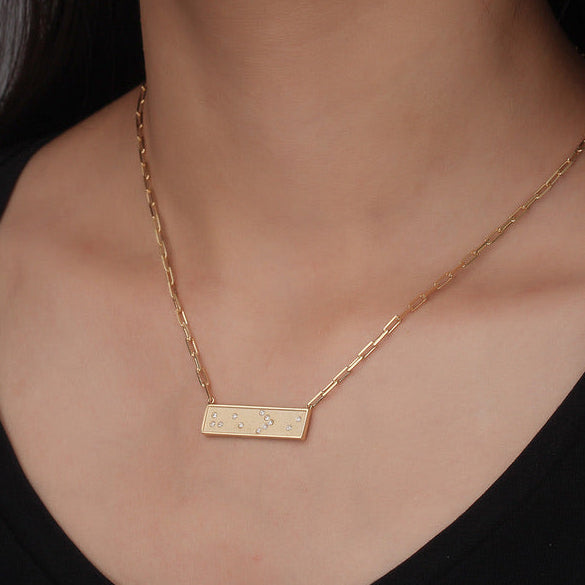 Gold Braille 'He is Greater Than I' He > i necklace with a bar pendant on a person wearing a black top against a neutral background