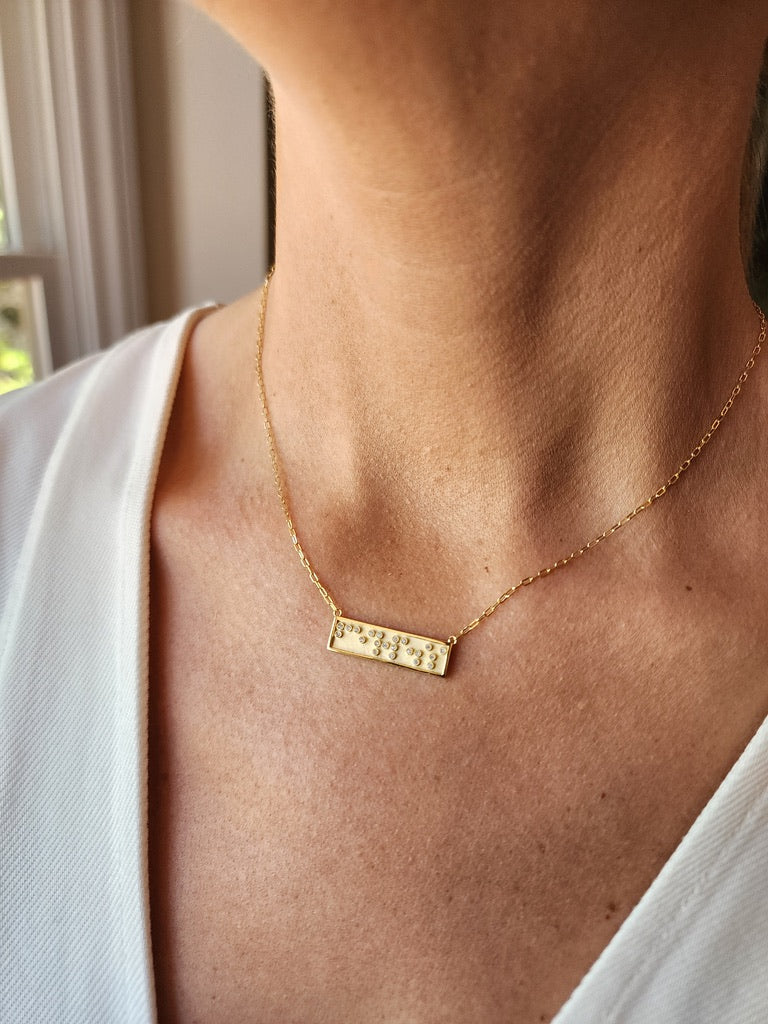 Gold mini bar necklace with Fearless in Braille crystals on a model