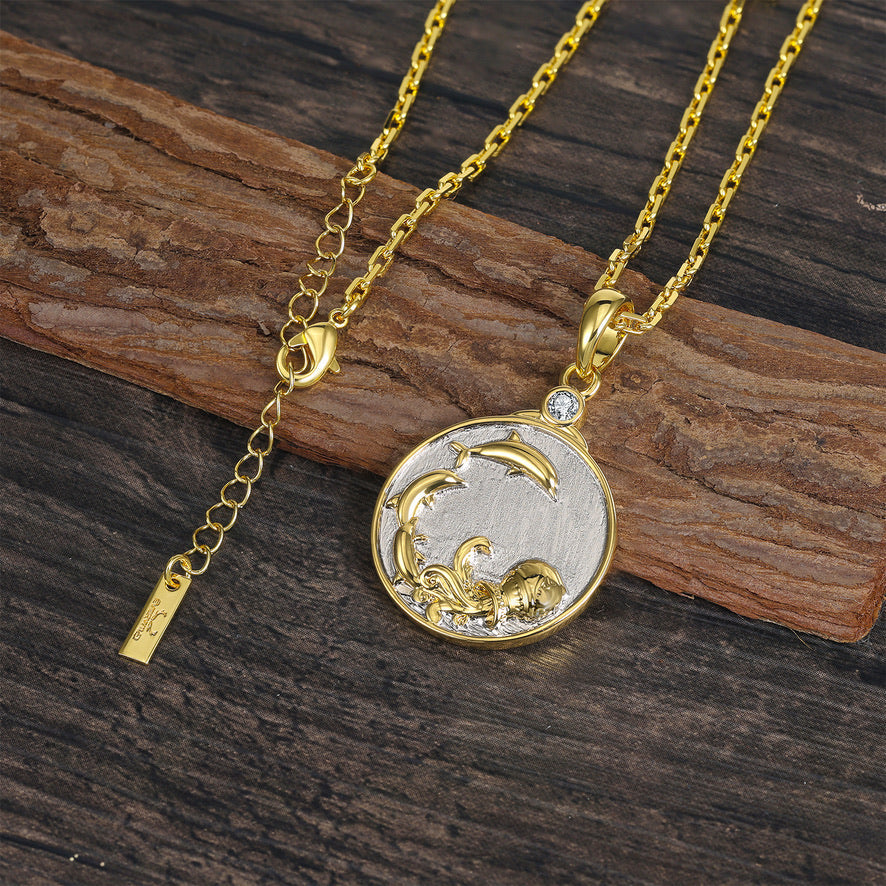 Gold and silver Aquarius Zodiac pendant necklace with a water urn and leaping dolphins shown on a wooden surface