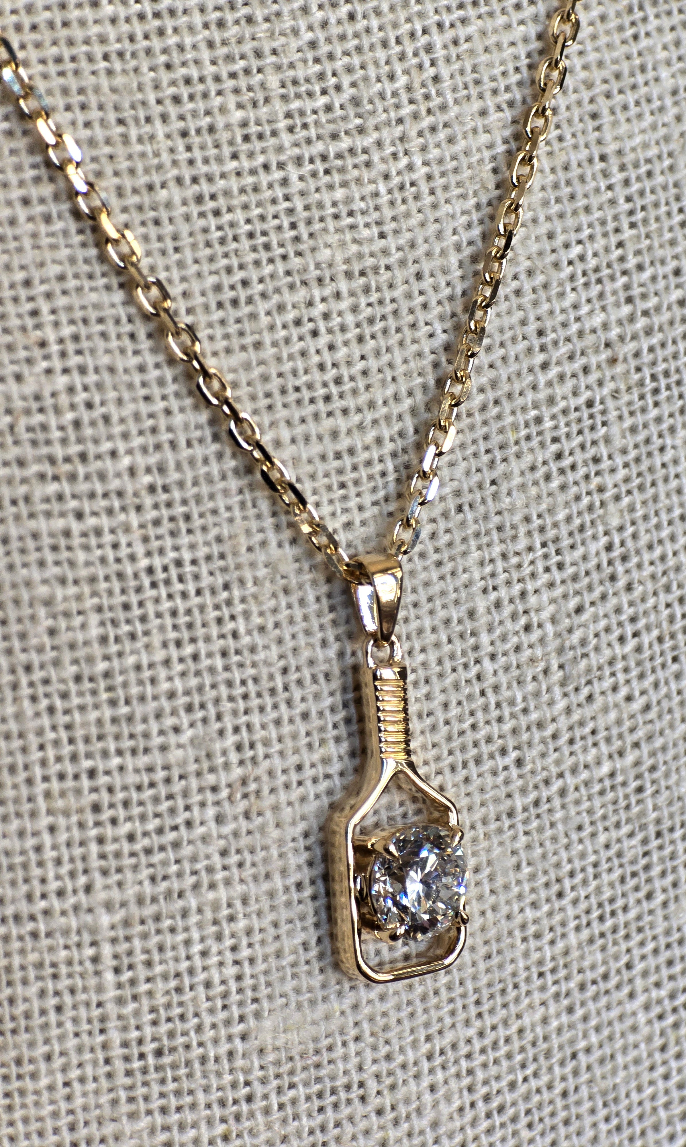 Gold necklace with a pendant featuring a diamond on a textured gray background