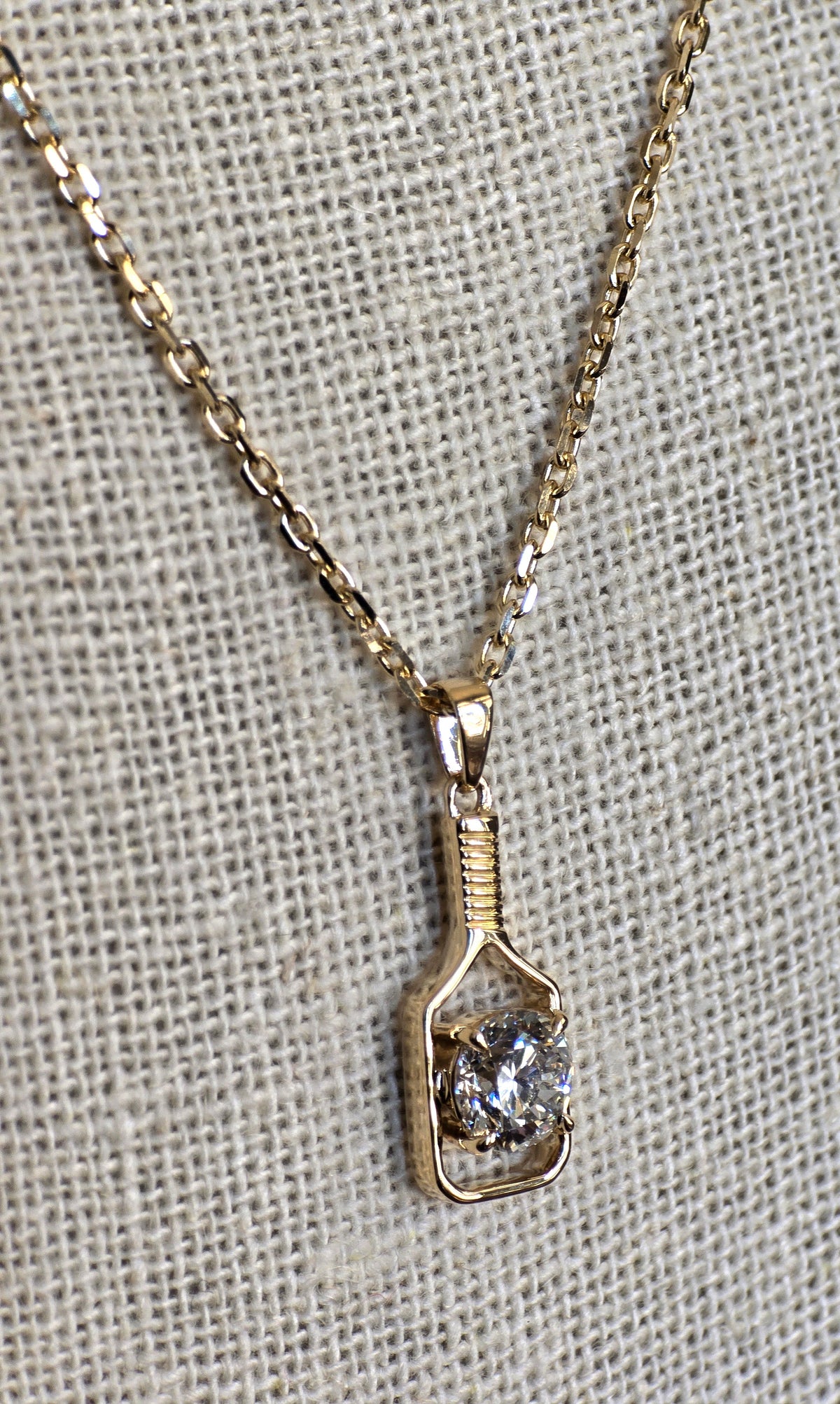 Gold necklace with a pendant featuring a diamond on a textured gray background