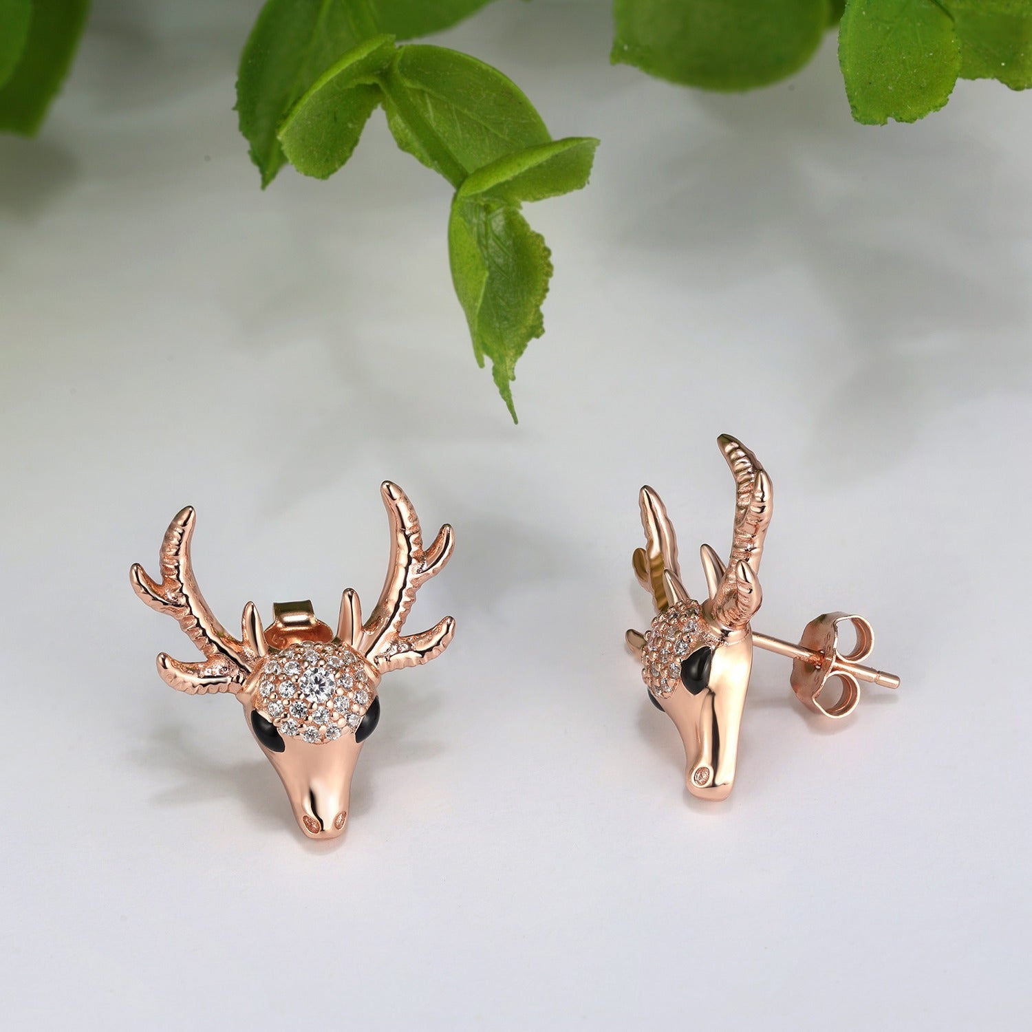 Rose gold deer head earrings with antlers and crystals on a white background.