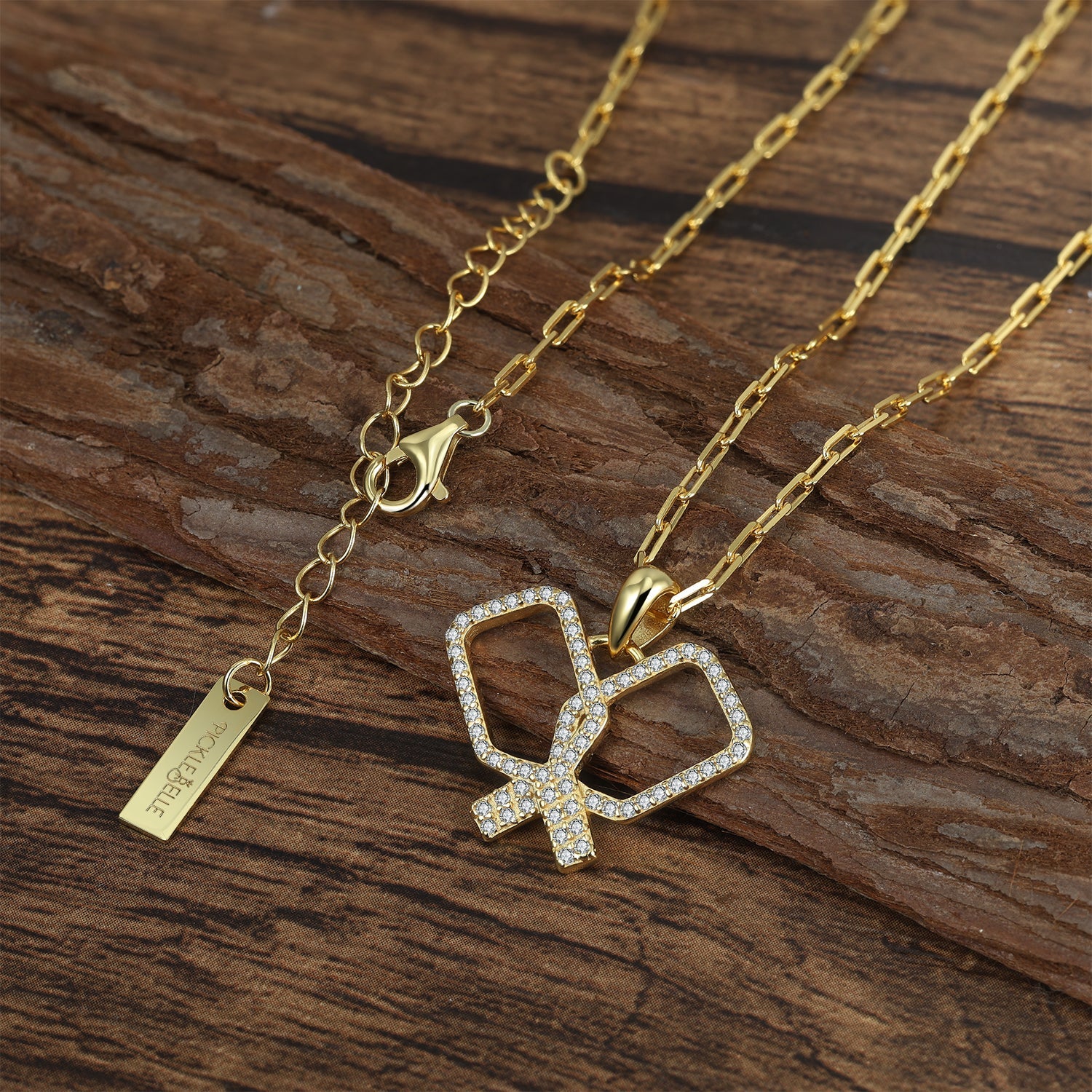 Gold necklace with criss crossing crystal pickleball paddles pendant on a wooden surface
