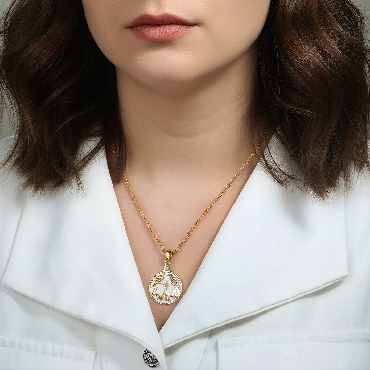 Woman wearing a gold and silver necklace with a Libra Zodiac pendant against a neutral background