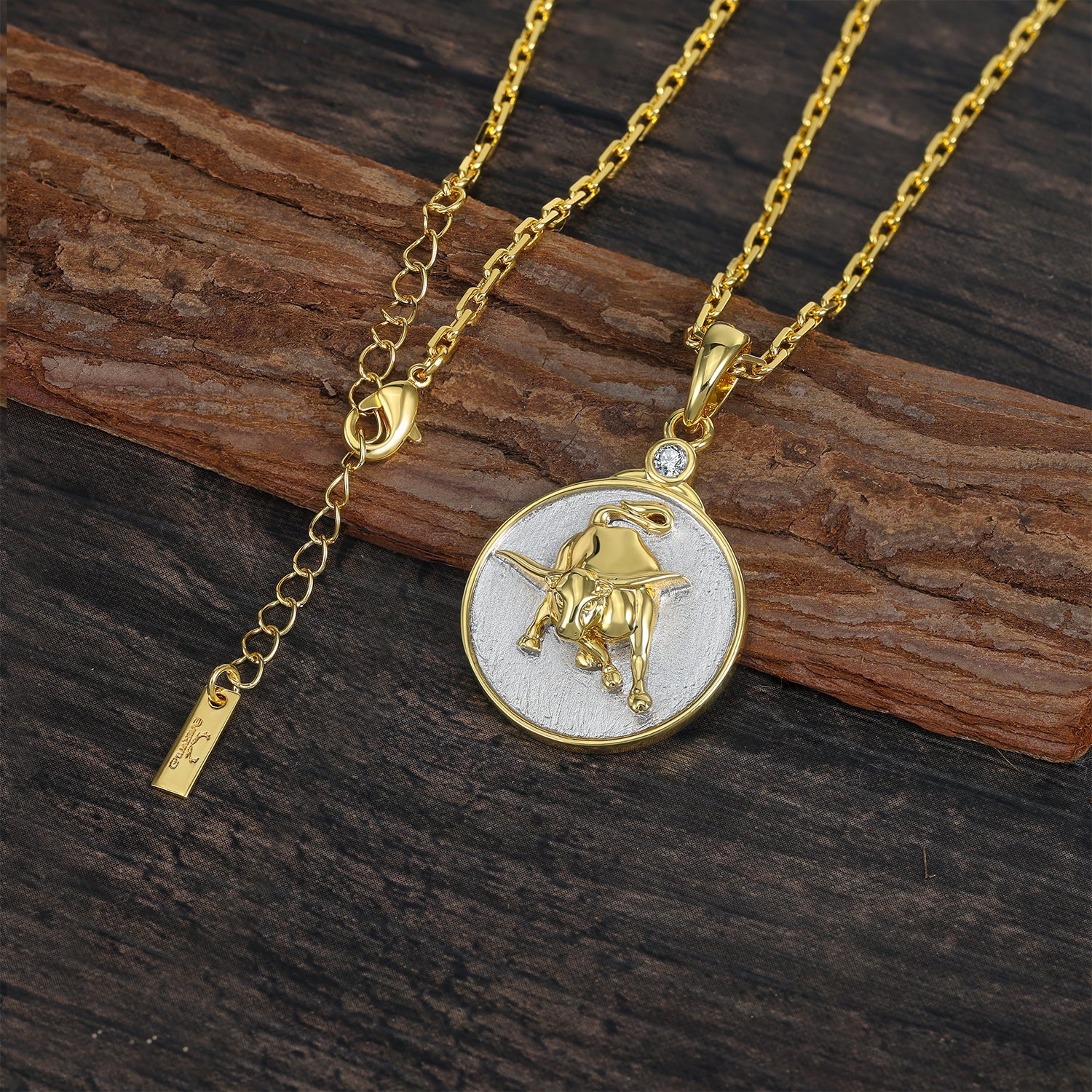 Gold necklace with a Gold and Silver pendant featuring a TAURUS Zodiac bull design on a wooden surface