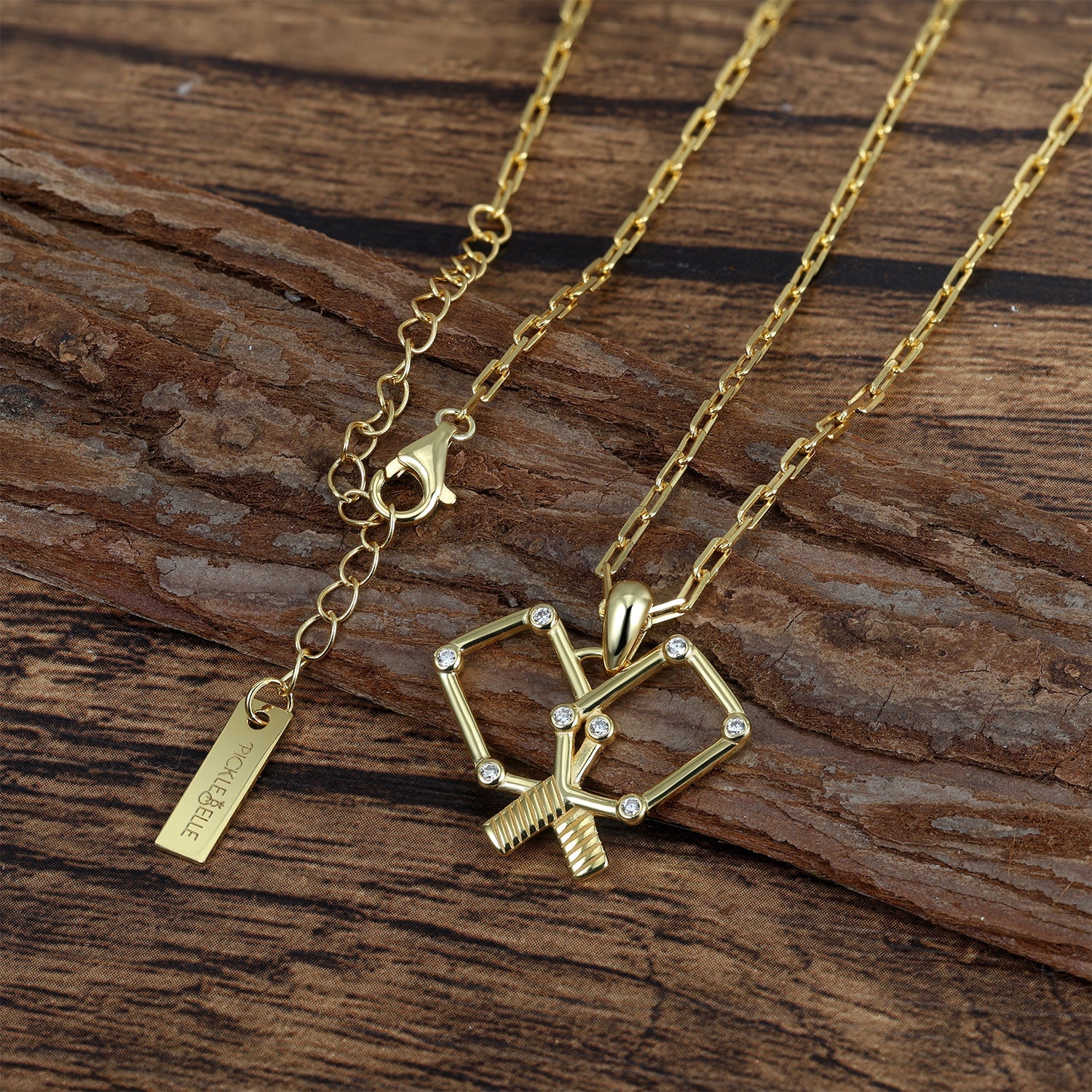 Gold necklace with a pickleball crossed paddles pendant on a wooden surface