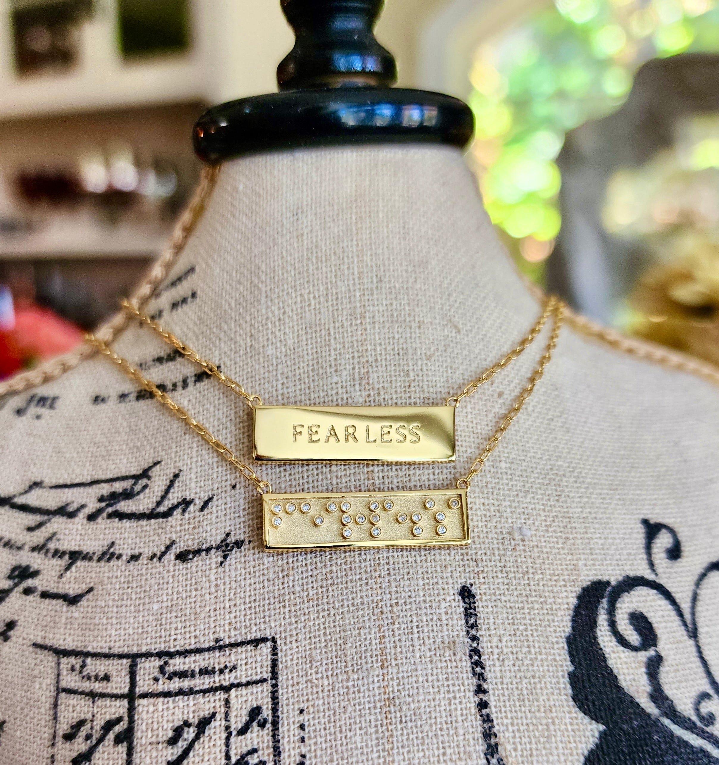 Gold necklace with 'FEARLESS' in Braille crystals and text pendant on a mannequin bust