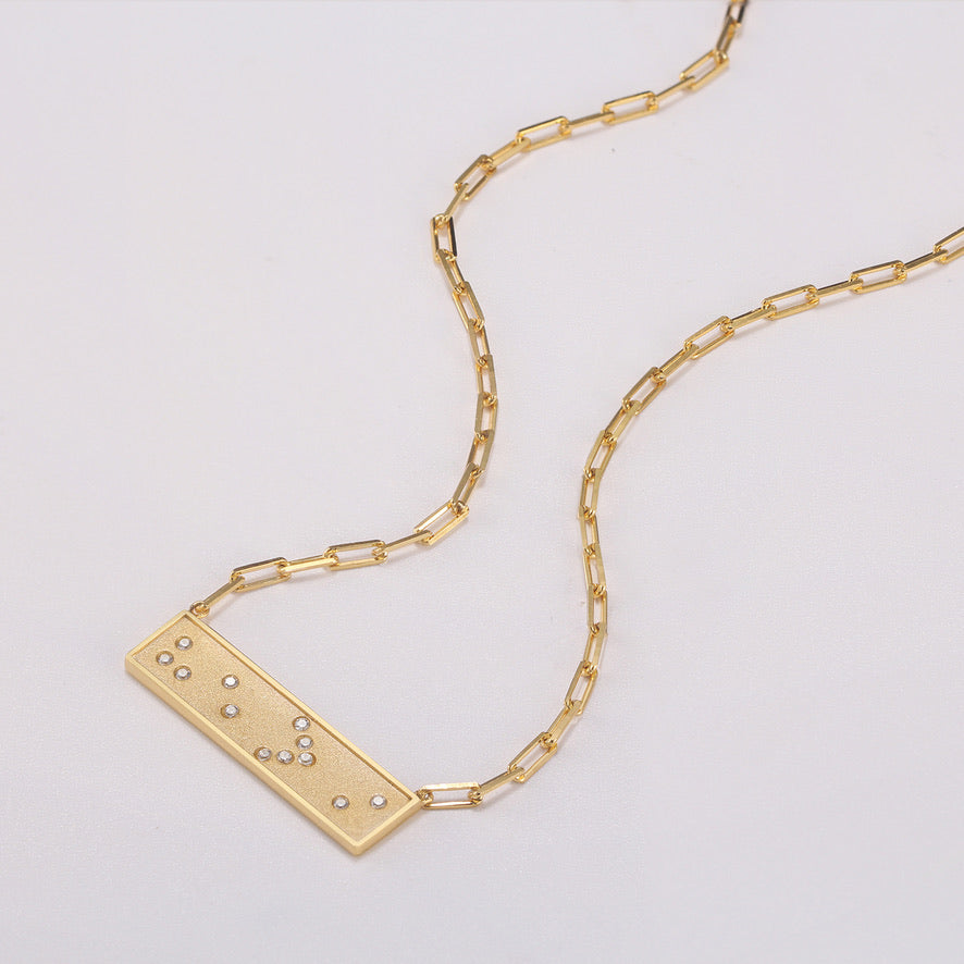 Gold necklace with a horizontal bar Braille crystal pendant on a white background He > i