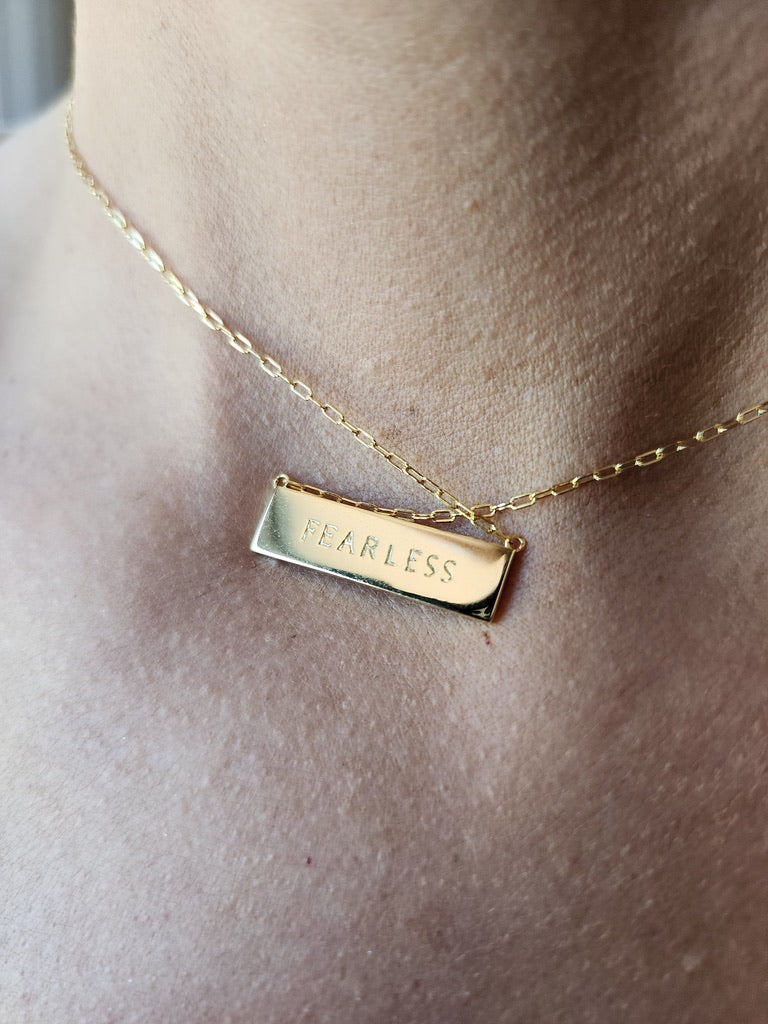 Gold necklace with 'FEARLESS' text pendant on a model