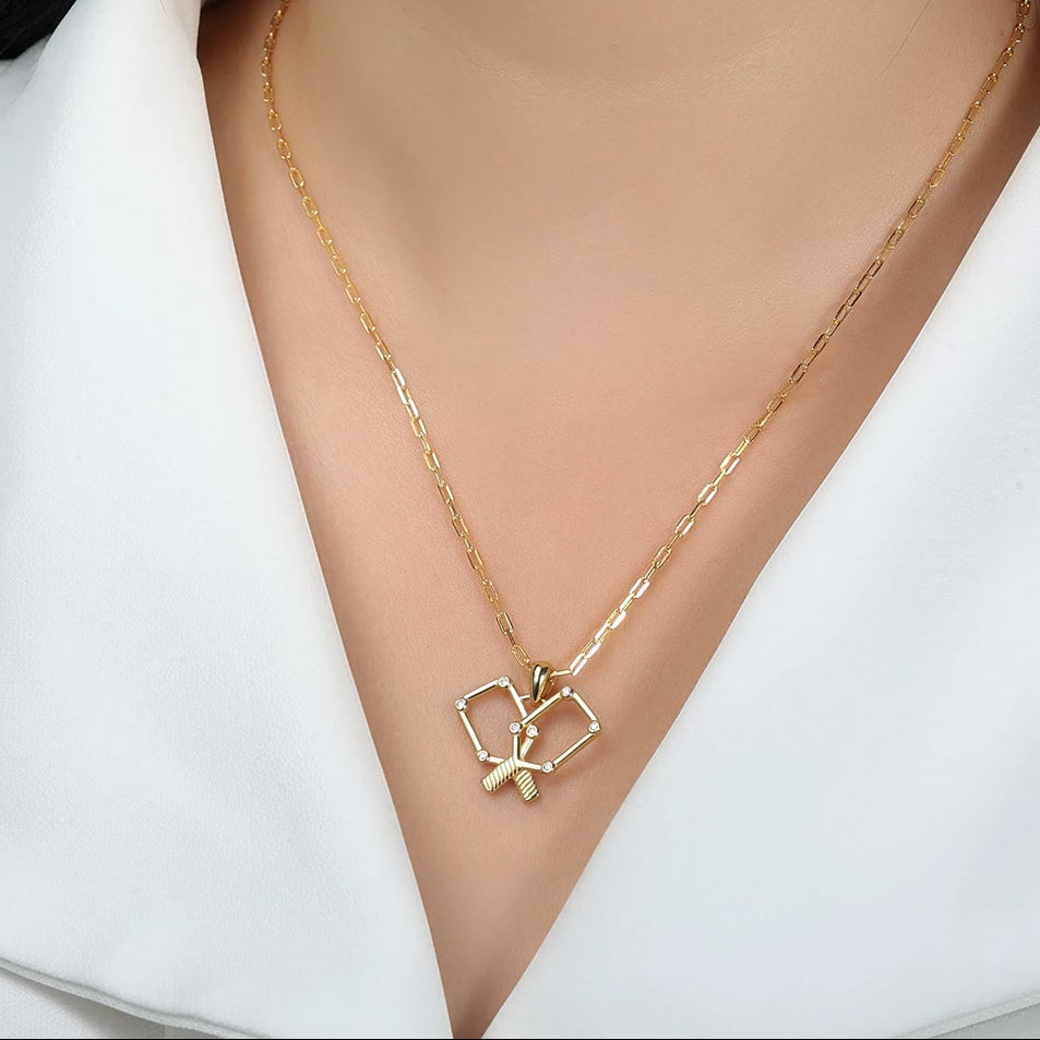 Gold necklace with a pickle ball paddle pendant on a model wearing a white shirt.