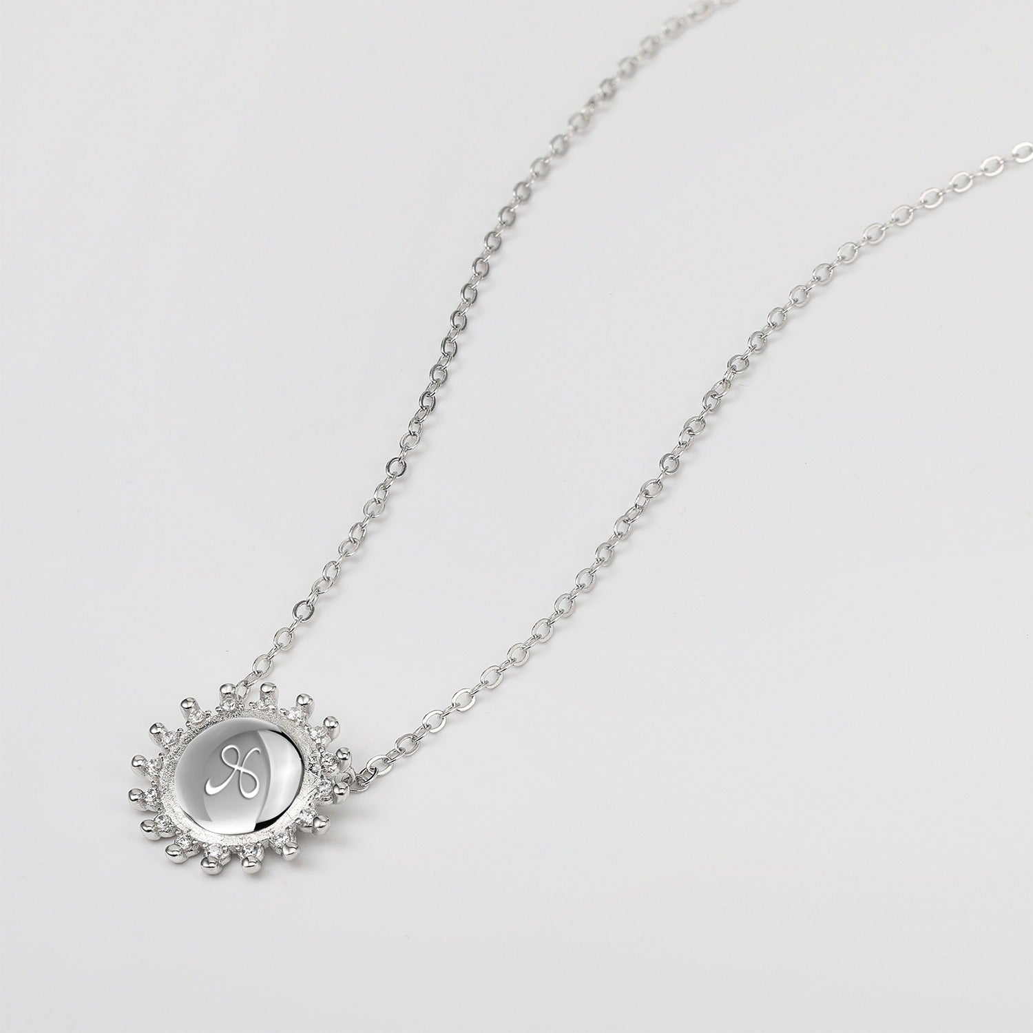 Silver necklace with a circular sunburst pendant with etched friendship symbol on a white background