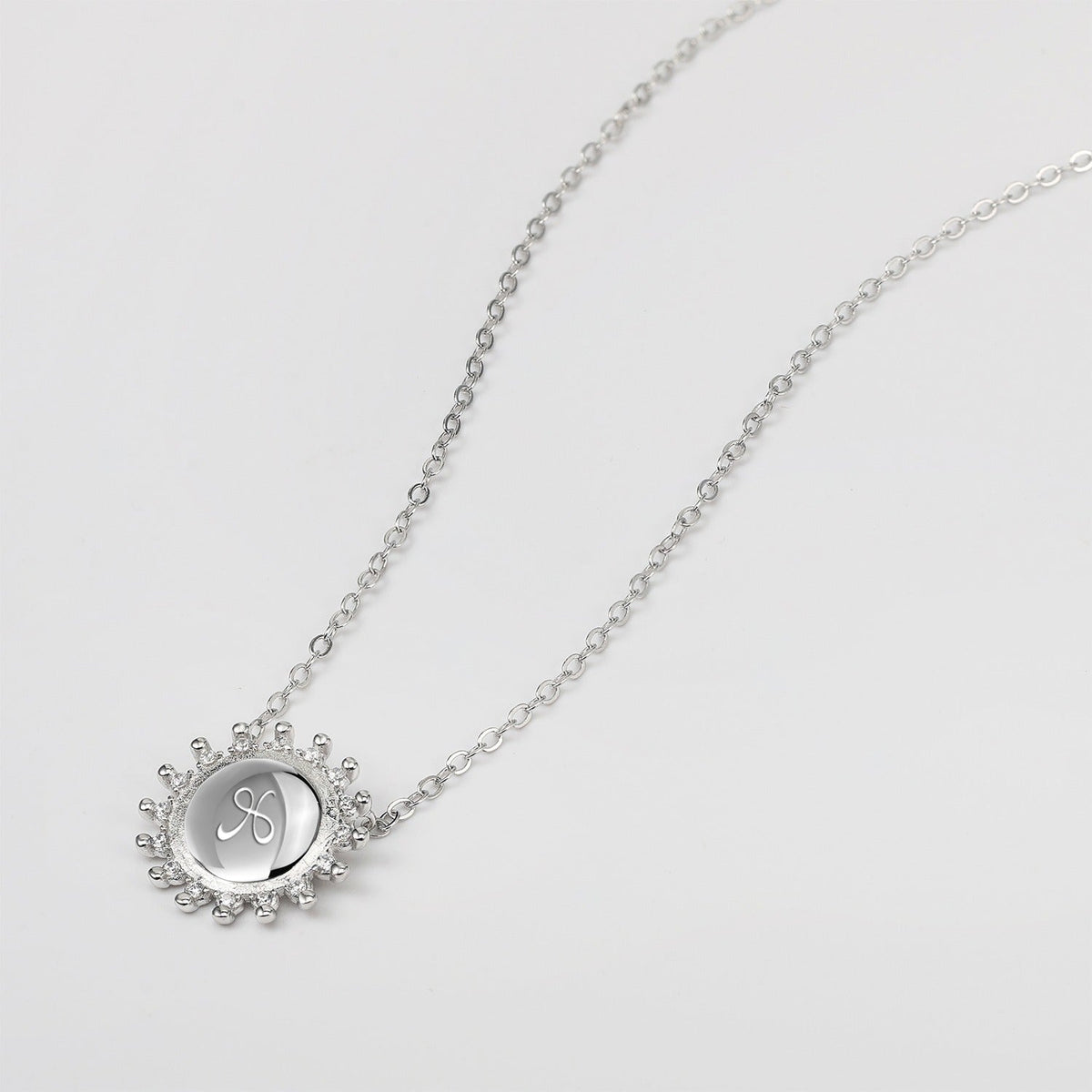 Silver necklace with a circular sunburst pendant with etched friendship symbol on a white background