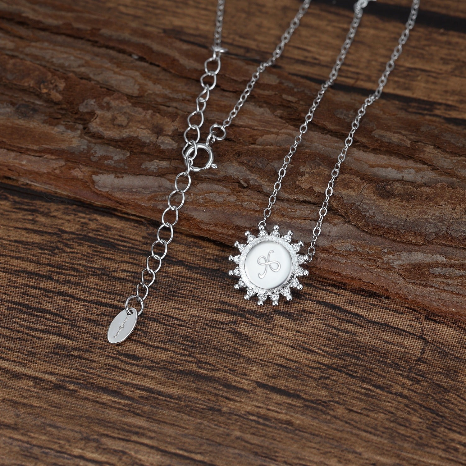 Silver necklace with a sun-shaped pendant etched with the friendship symbol on a wooden surface