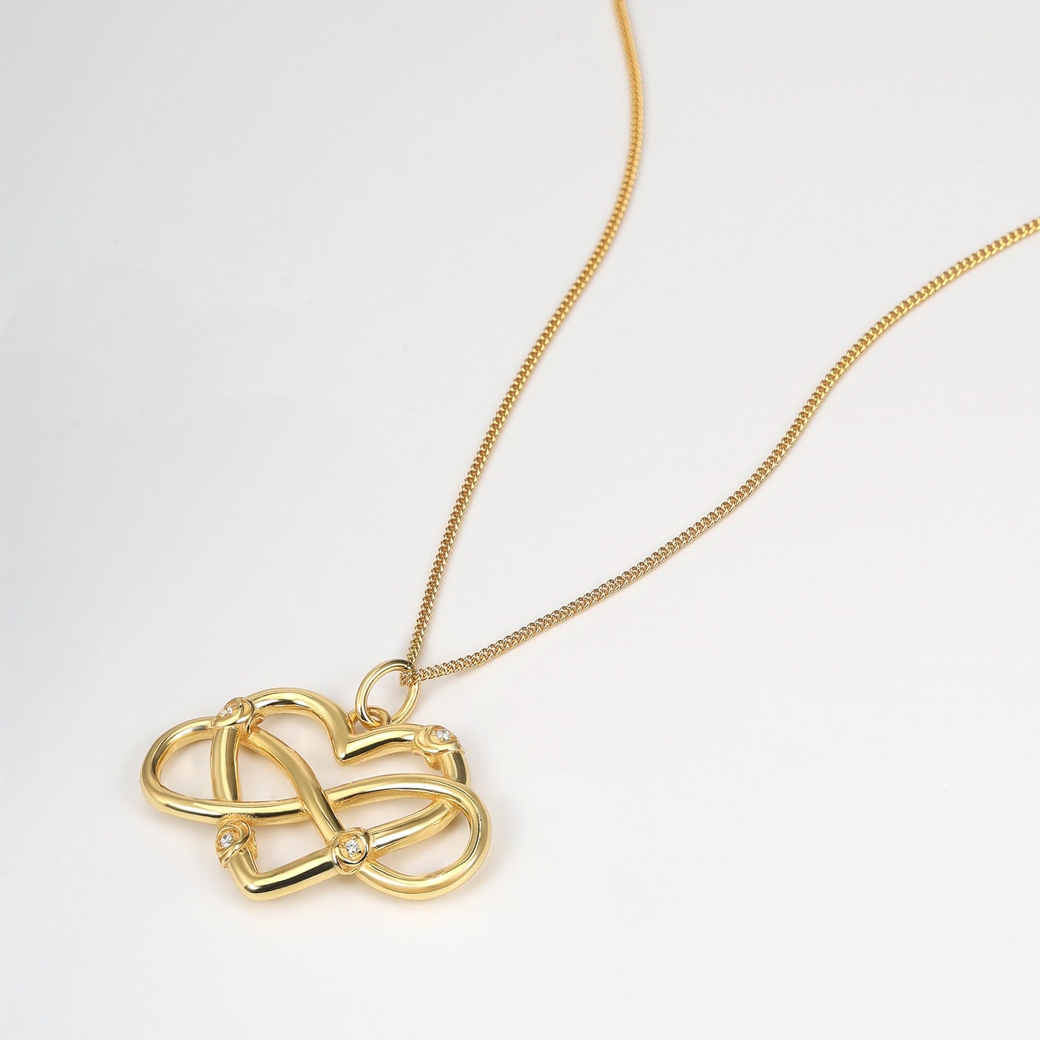 Gold necklace with a heart-shaped and infinity symbol pendant on a white background