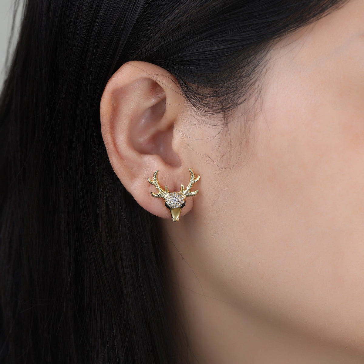 Gold deer head earring worn by a person with dark hair.