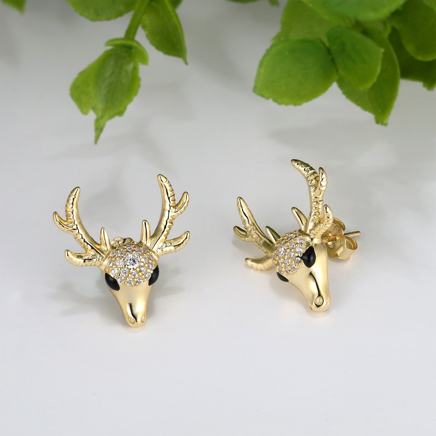 Gold deer head earrings with antlers gemstones on a light background.