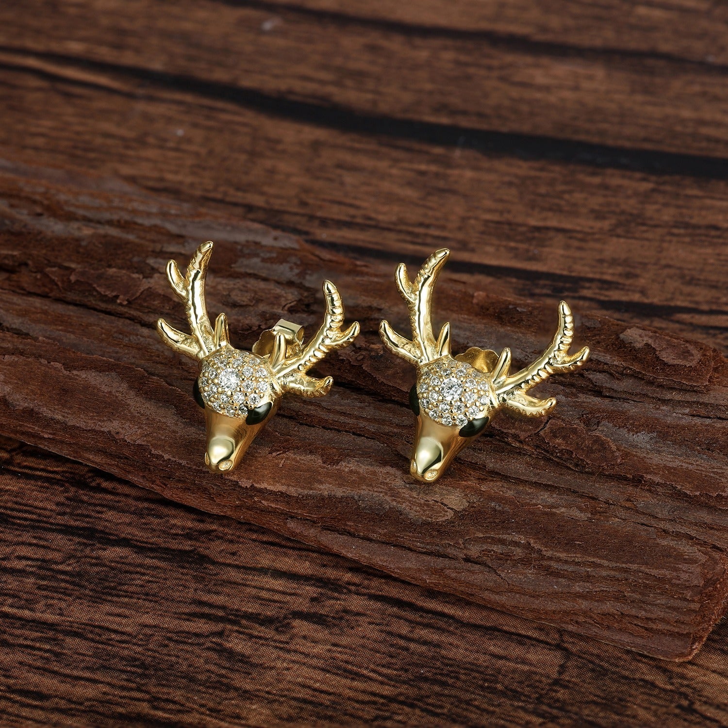 Gold deer head earrings with antlers and gemstones on a wooden surface