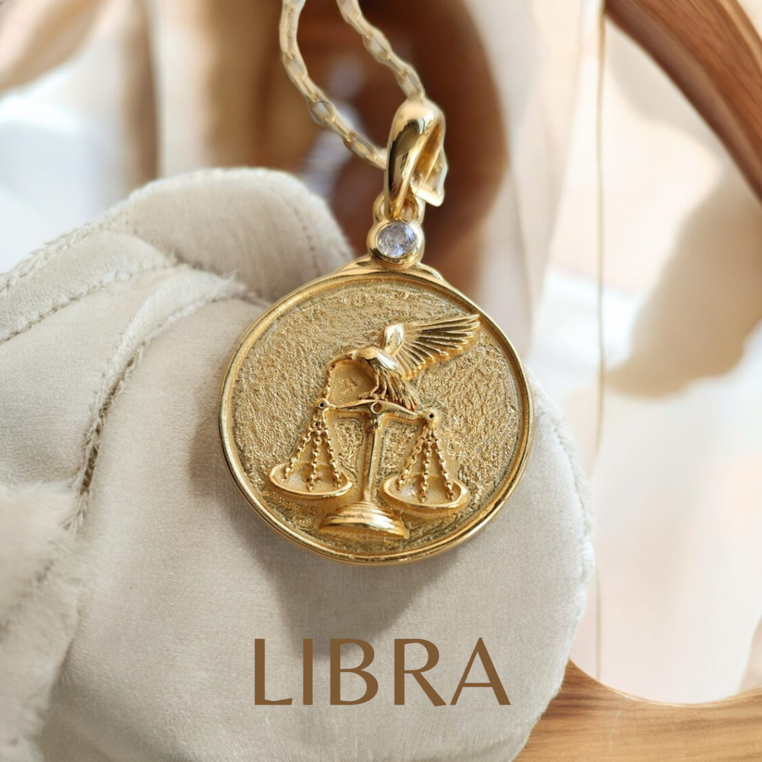 Gold Libra zodiac pendant depicting a raven on a scale on a soft fabric background