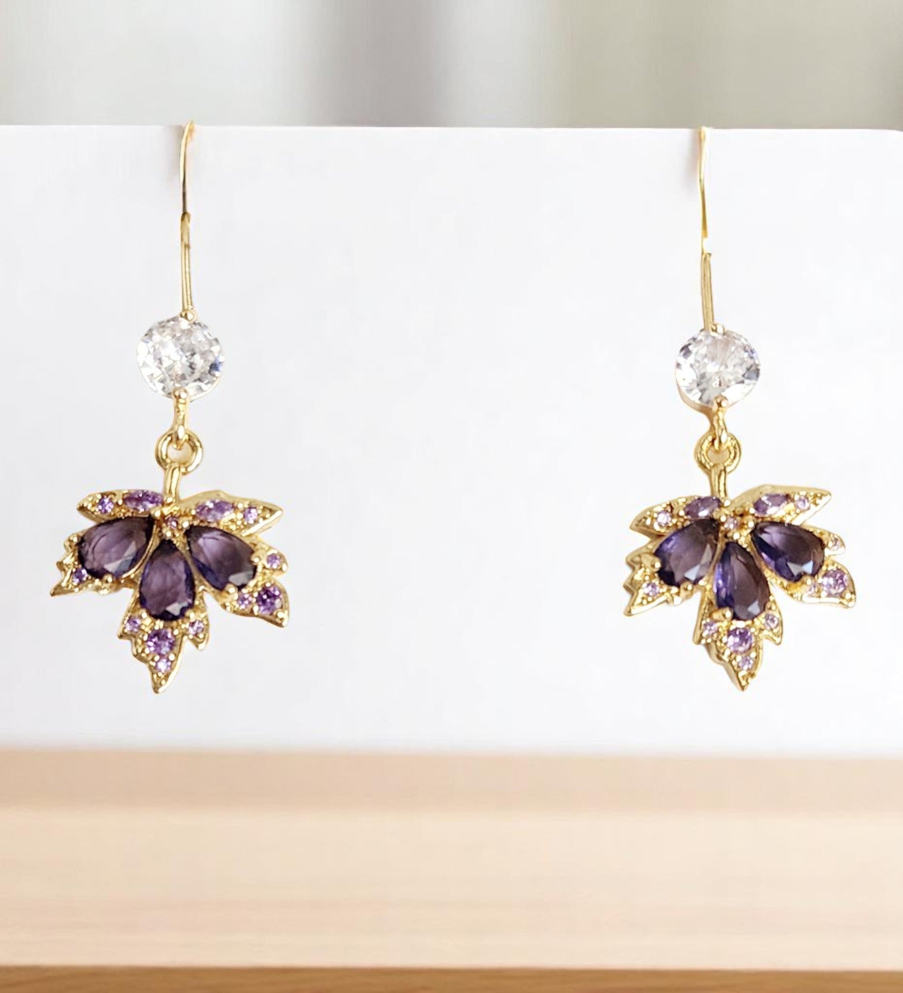 Gold maple leaf earrings with purple and clear gemstones on a white background
