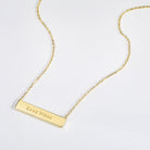 Gold necklace with a bar pendant that is engraved with the text 'Good Vibes' on a white background