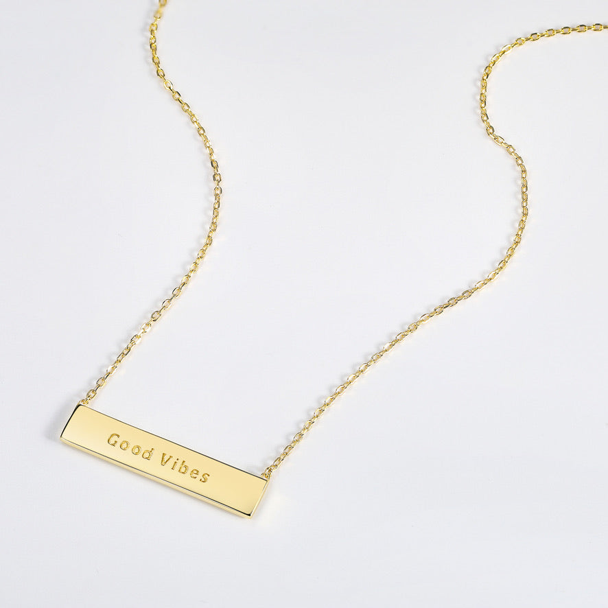 Gold necklace with a bar pendant that is engraved with the text 'Good Vibes' on a white background
