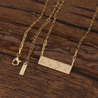 Gold Braille message necklace with a rectangular pendant on a wooden surface