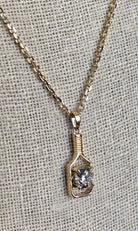 Gold necklace with a pendant featuring a diamond on a textured gray background