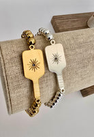 Two Picklebelle beaded stretch bracelets with pickleball paddle charms on linen display one each silver and gold