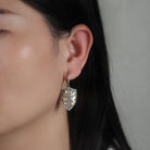 Close-up of a person wearing a decorative antique gold earring with a decorative shield design.