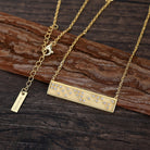 Gold necklace with a bar pendant and Good Vibes in Braille crystals on a wooden surface
