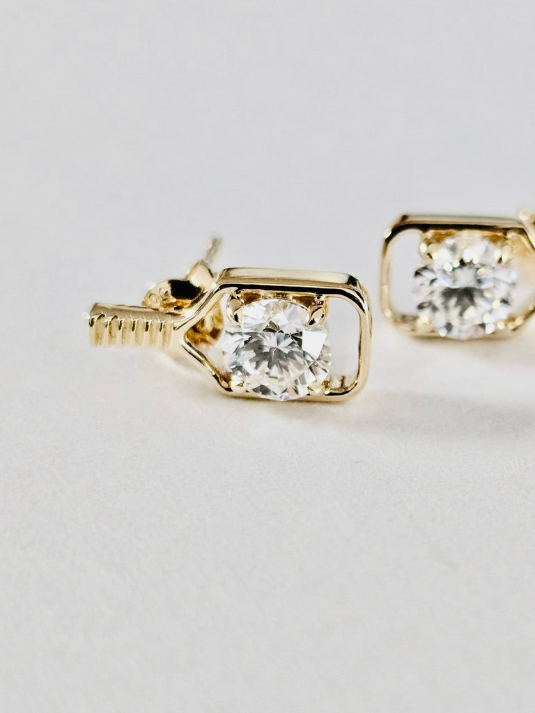 solid gold pickleball paddle stud earrings with a square bezel setting and a clear round-cut diamond, shown on a light neutral background.