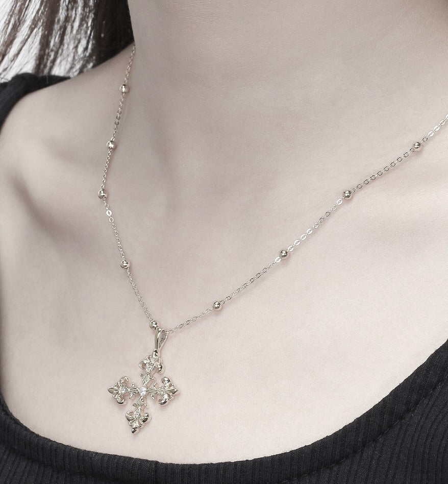 Saints and Saviors Silver necklace with a four-sided fleur de lis pendant worn by a person against a neutral background