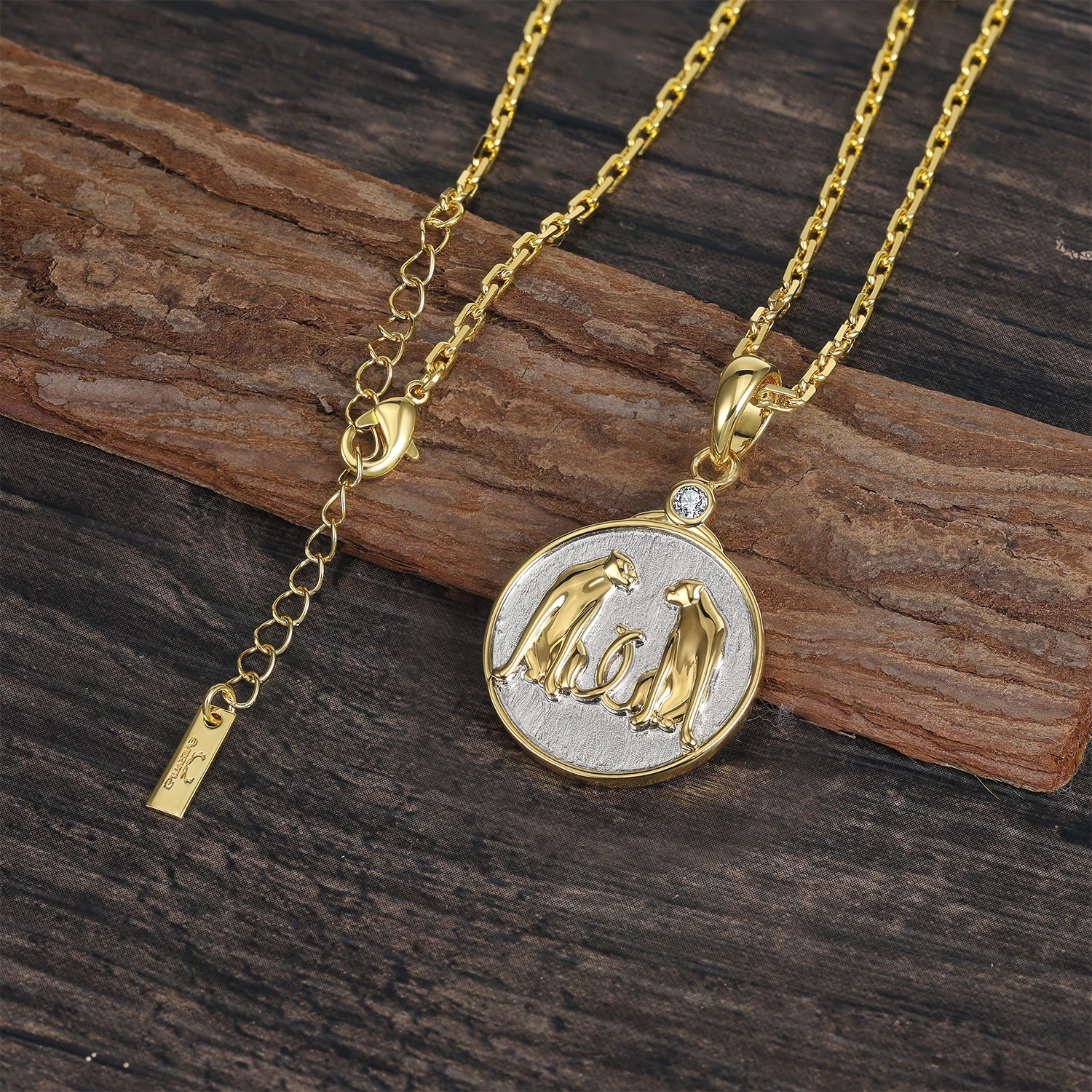 Gold and silver necklace with a Zodiac Gemini pendant featuring two leopards on a wooden surface