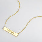 Gold necklace with a bar pendant displaying the word 'limitless' on a light gray background