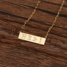 Gold necklace with 'HE>I' pendant on a wooden surface
