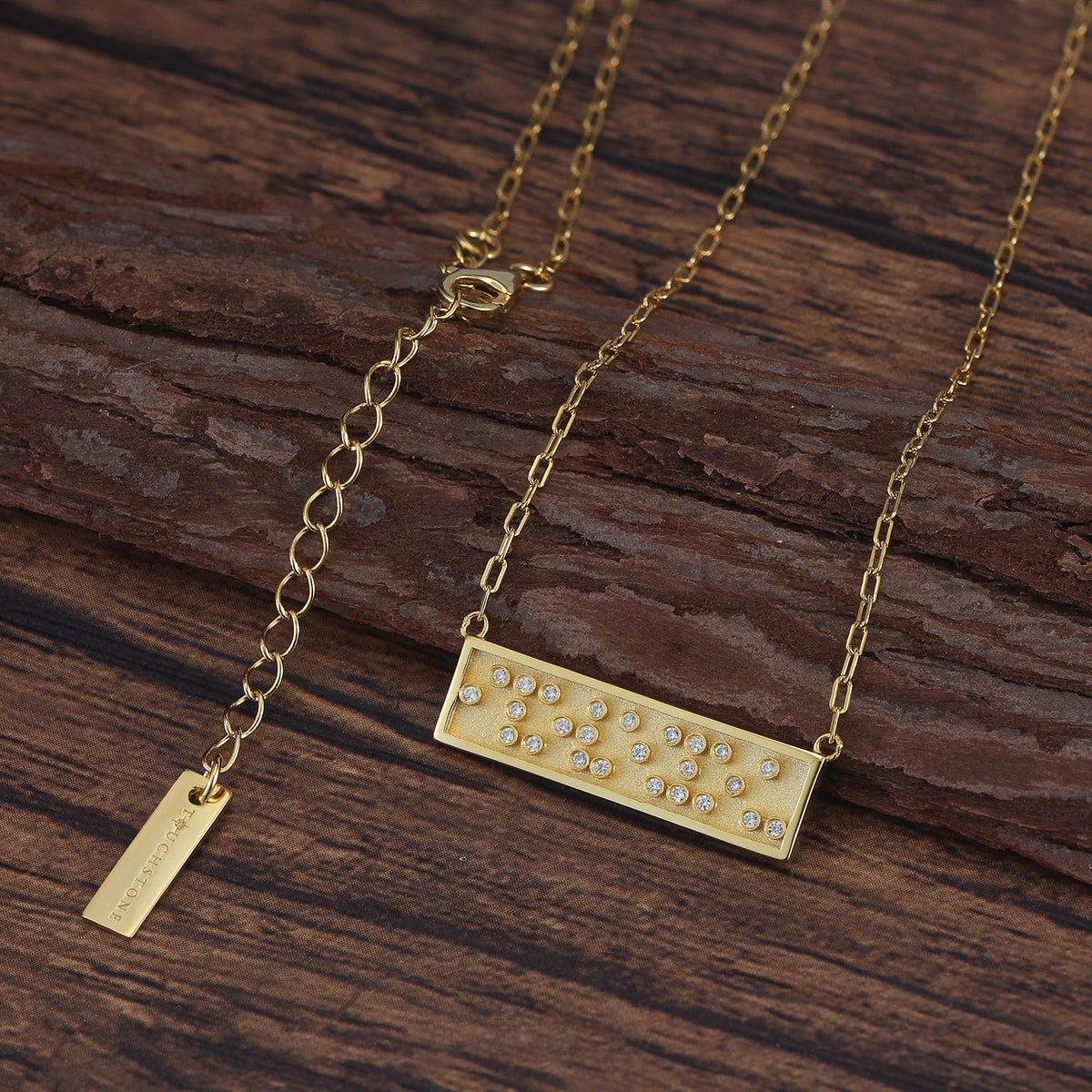 Touchstone I Love You Mini-Bar Necklace in Gold with Braille 'I Love You' in Crystals on wood surface
