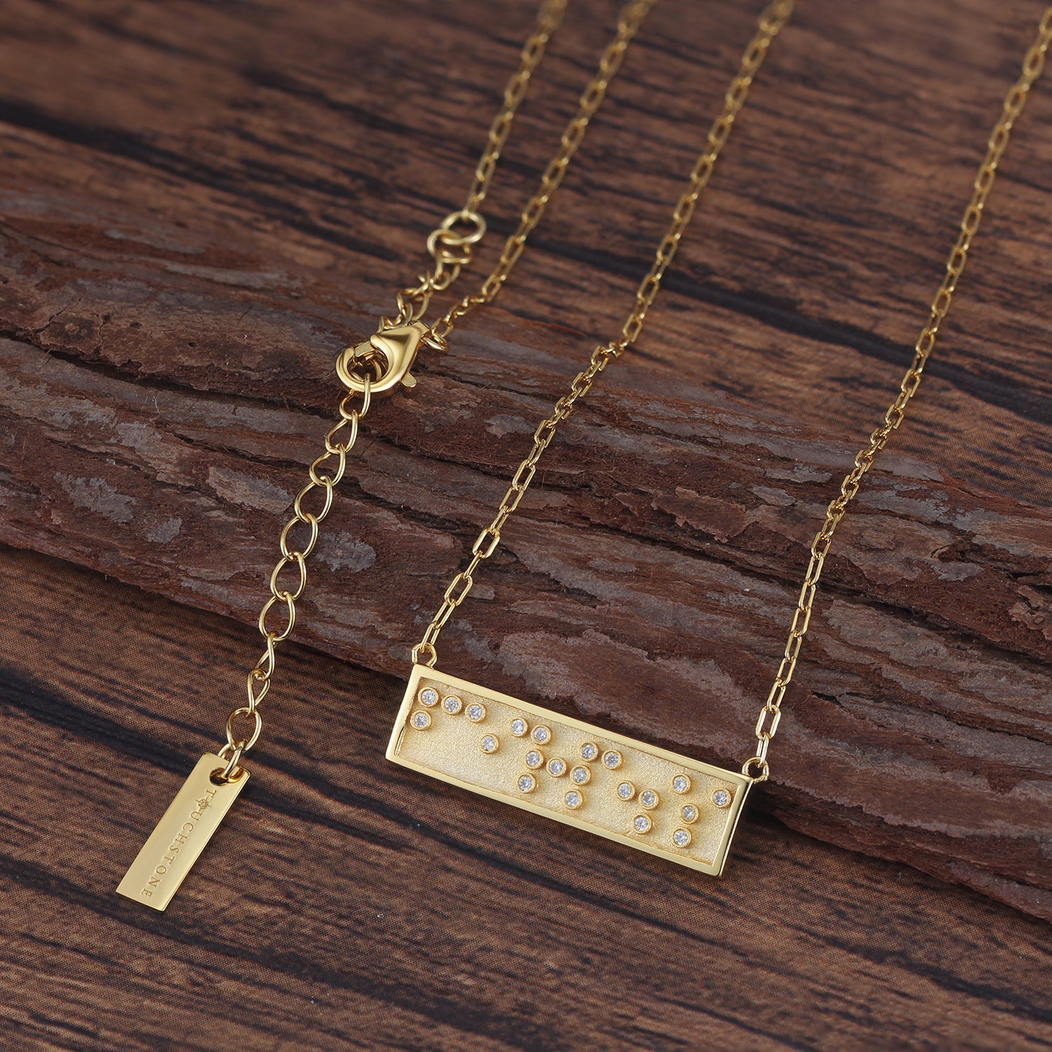 Touchstone Fearless Mini-Bar Necklace in Braille crystals in Gold on a wooden background