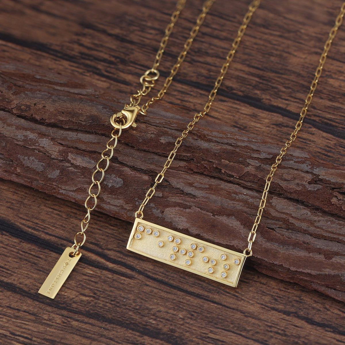 Touchstone Fearless Mini-Bar Necklace in Braille crystals in Gold on a wooden background