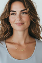 Woman wearing a Solid Gold Tennis and Ball gold necklace against a plain background