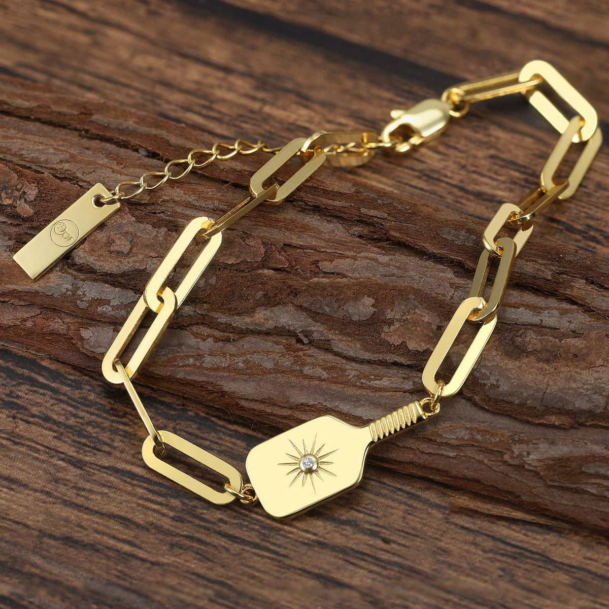 Gold bracelet with decorative pickleball paddle design and clip links on a wooden surface
