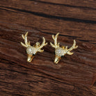 Gold deer head earrings with antlers and gemstones on a wooden surface
