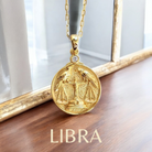 Gold Libra zodiac pendant necklace on a wooden surface with a blurred background